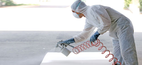 A person in white suit and mask painting a wall.